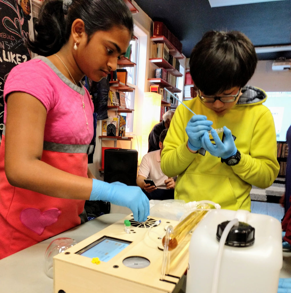 Kids doing genetic engineering at Cambridge Science Festival using Amino Labs' BioExplorer minilab, desktop biolab, a biohacker lab, DIY bio lab, laboratory equipment for glowing bacteria, e.coli bacteria, STEM science project, home lab, biotechnology lab, home science lab, school science lab, biohacking lab, iGEM, DIY biology, bio production, bacterial transformation lab, genetic engineering