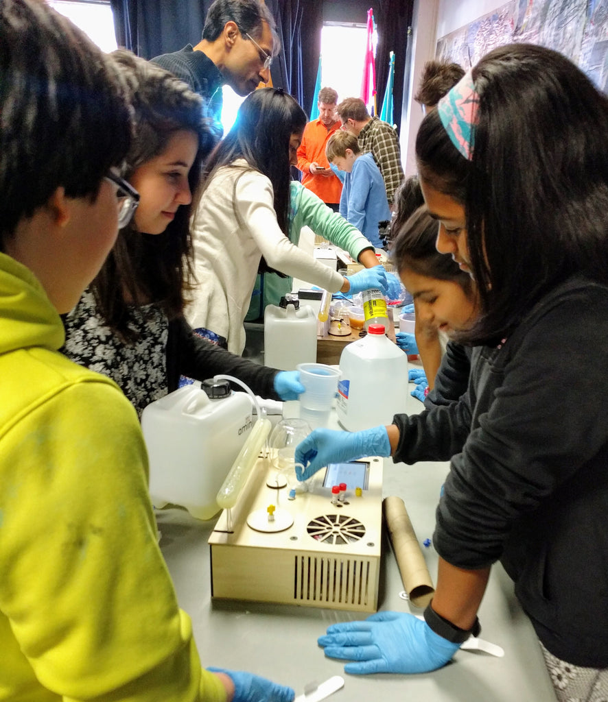 Kids doing genetic engineering at Cambridge Science Festival using Amino Labs' BioExplorer minilab, desktop biolab, a biohacker lab, DIY bio lab, laboratory equipment for glowing bacteria, e.coli bacteria, STEM science project, home lab, biotechnology lab, home science lab, school science lab, biohacking lab, iGEM, DIY biology, bio production, bacterial transformation lab, genetic engineering