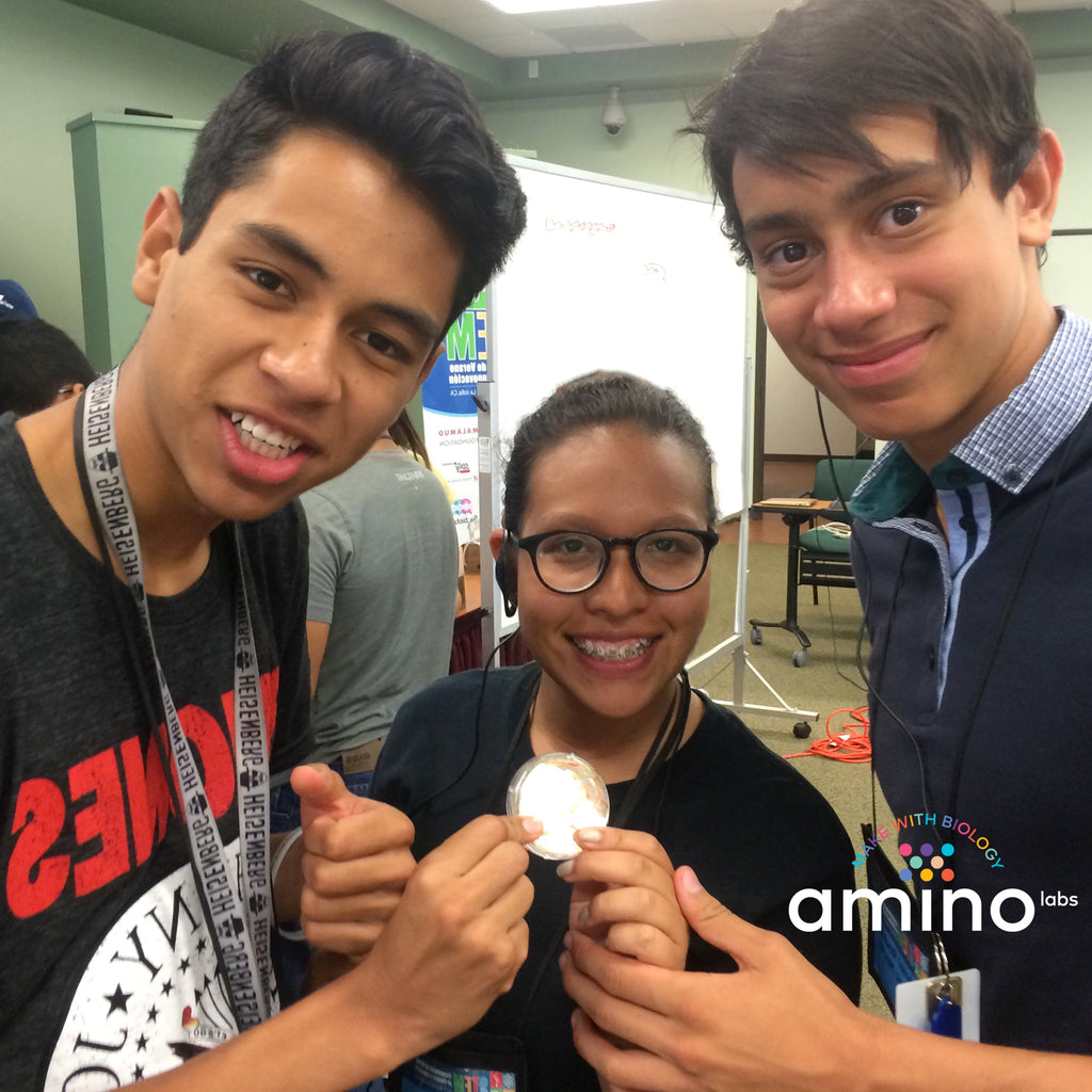 students holding a petri dish of genetically engineered bacteria made with Amino Labs’ Zero to Genetic Engineering hero starter pack for  middle school science, biology, genetics, high school science, biology, genetics, NGSS.  Learn what is DNA, what is a gene, cell theory, genetic engineering, bioart, biotechnology, biohacking and genetic engineering with the world's first biohacking and biotechnology STEM beginner's book and starter pack of science project kits, biotechnology project kits