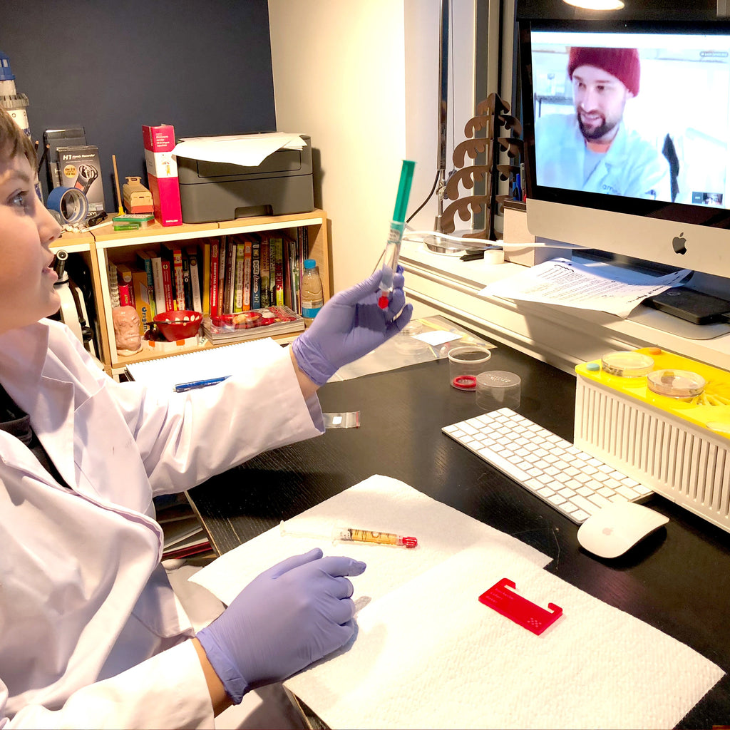 young student in lab coat showing a syringe to a scientist during a Genetic Engineering DIY biohacking virtual lessons by Amino labs STEM biotechnology kits and school laboratory equipment / home laboratory equipment / biohacking laboratory equipment